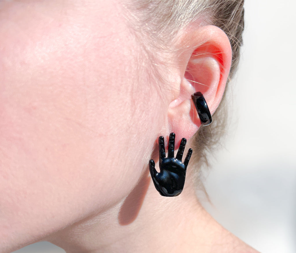 left hand shaped stud earring in black enamel with palm facing outward and black ear cuff on ear