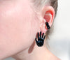 Chunky goth black ear cuff on ear with goth black hand earring palm facing forward. Hand-painted enamel.