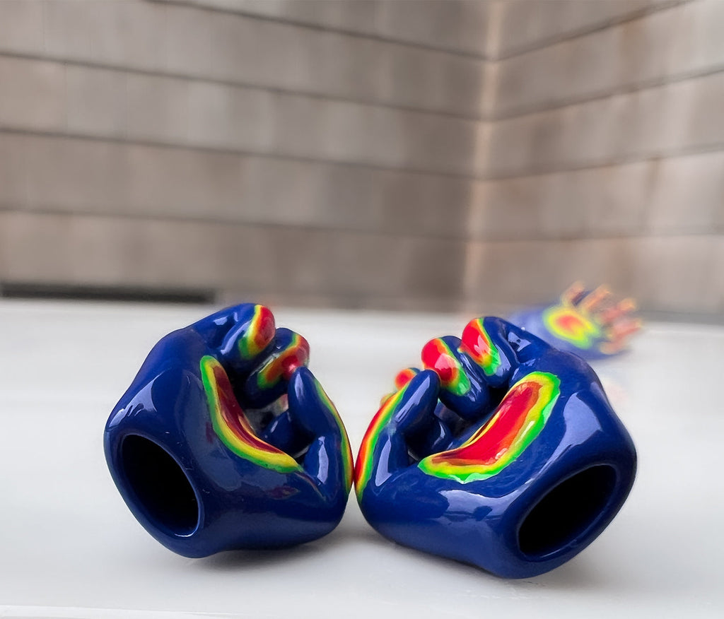 right and left middle finger stud earrings laying down to show that they are hollow. middle finger stud earrings in blue, with the fingers colored in as green, orange, yellow, and red. rainbow colored middle finger earring 