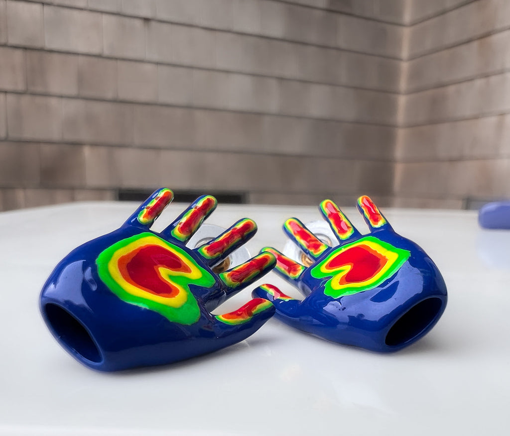 right and left hand shaped finger stud earrings laying down to show that they are hollow. hand shaped finger stud earrings in blue, with the fingers  and palm colored in as green, orange, yellow, and red. rainbow colored middle finger earring