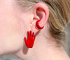 left hand shaped stud earring in red enamel with palm facing outward and red ear cuff on ear